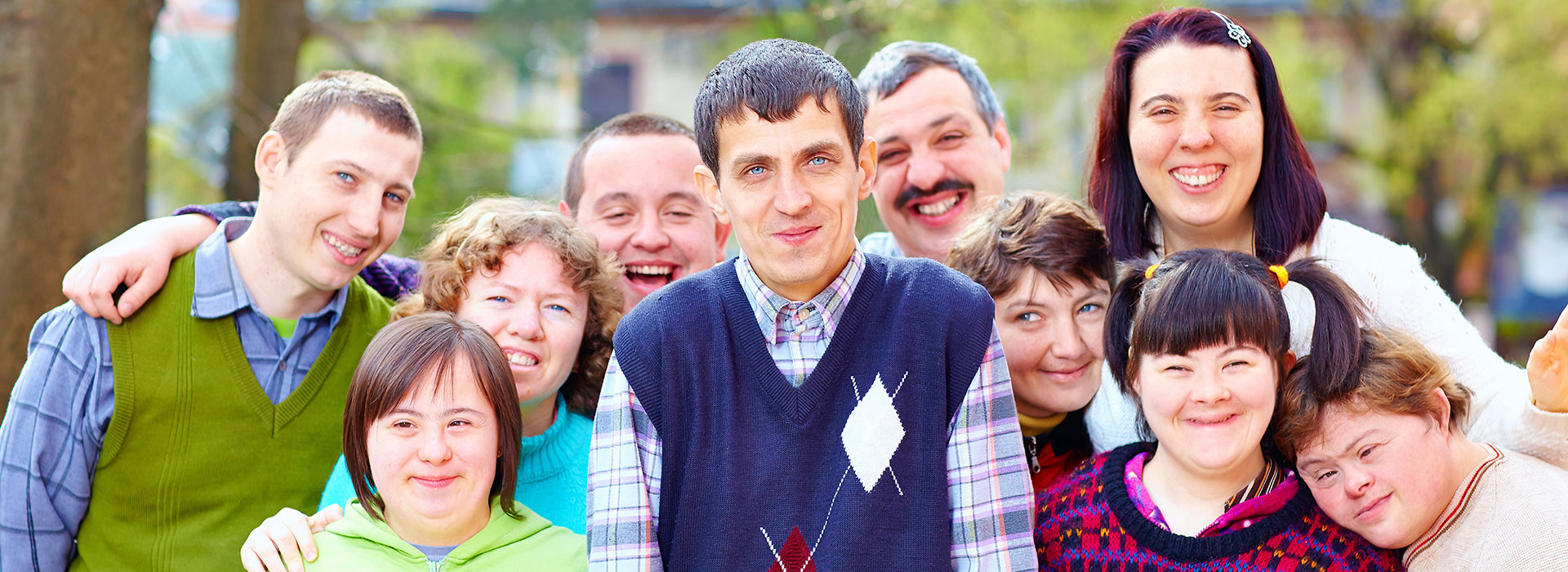 A group of young adults with developmental disabilities smiling together outdoors.